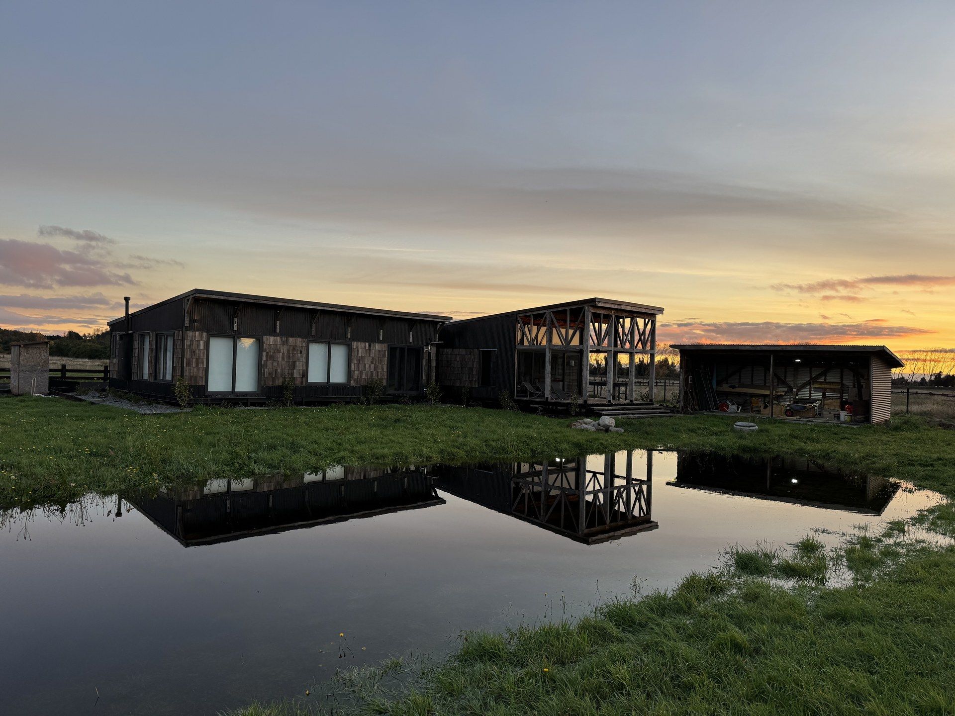 Casa de madera oscura al atardecer en el sur de Chile, reflejada en un espejo de agua